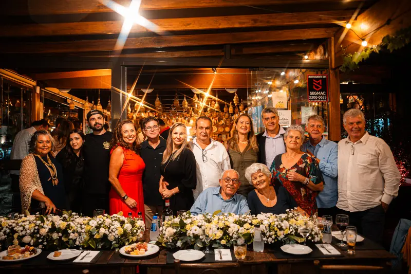 Convidados reunidos em volta da mesa enfeitada com flores, no salão da Cantina