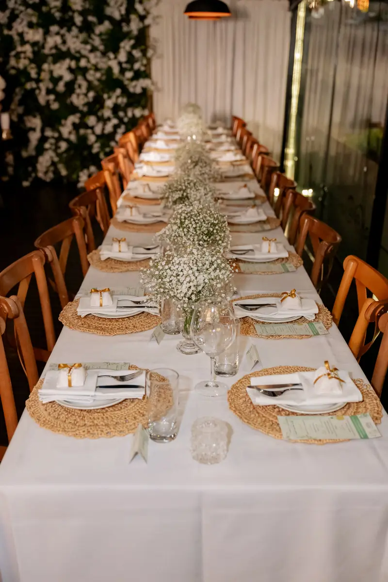 Mesa comprida posta para um casamento, com flores brancas e sousplats de palha